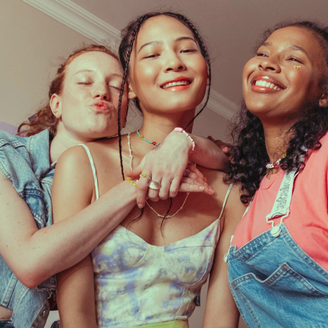 Three young girls with their arms around each other smiling at the camera